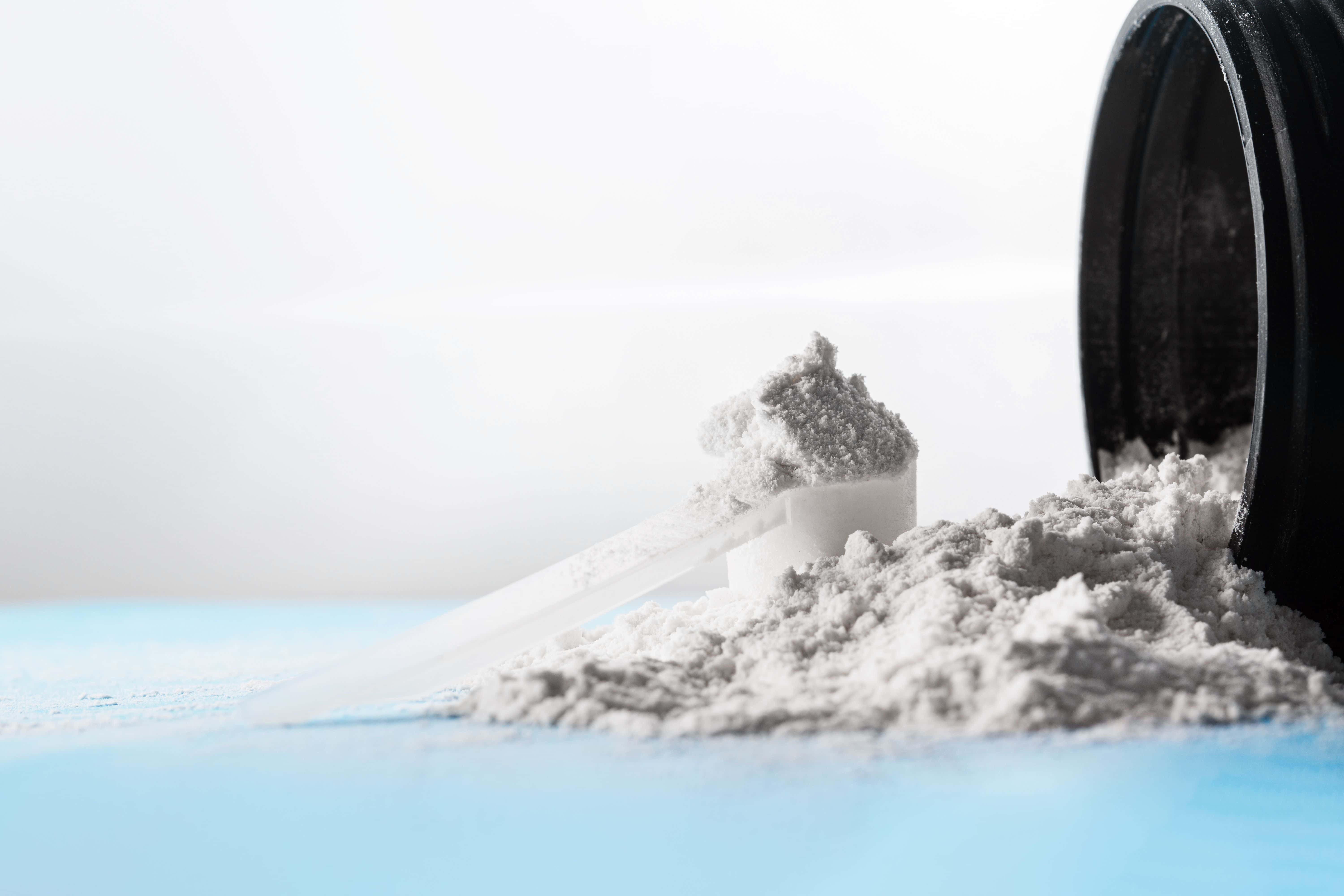 Closeup of a scoop of creatine powder on a scattered powder from the bottle on a blue surface